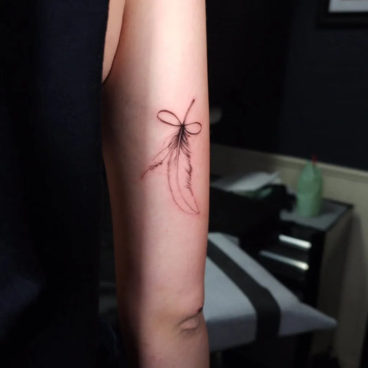 Small Fine Line Bow and Feather Tattoo on Women Arm by @girlstattooclubyeg