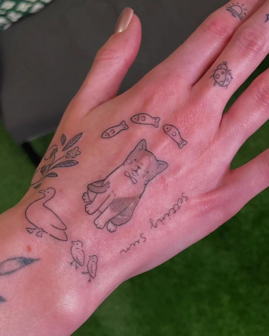 Small Fine Line Cat and Fish on Women Hand Tattoo by @arimika.tattoo