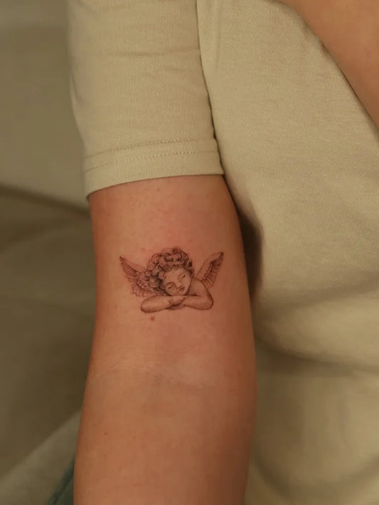 Small Fine Line Cherub Tattoo on Women Arm by @mayink.nl