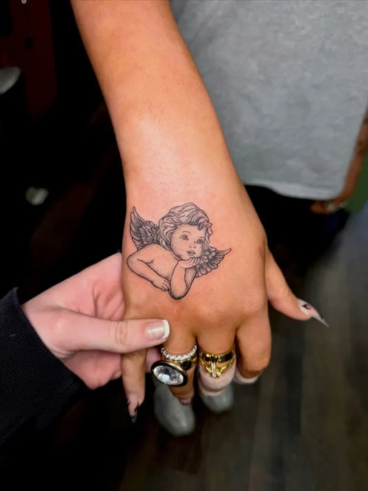 Small Fine Line Cherub Tattoo on Women Hand by @babyhandsbalfour