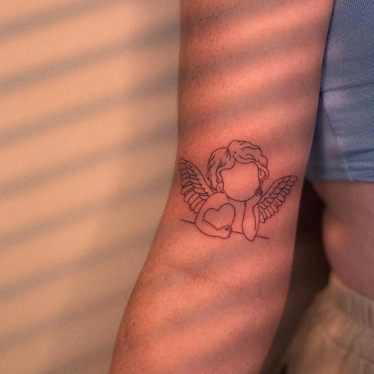 Small Fine Line Cherub with Heart Tattoo on Women Arm by @ellie_tatts