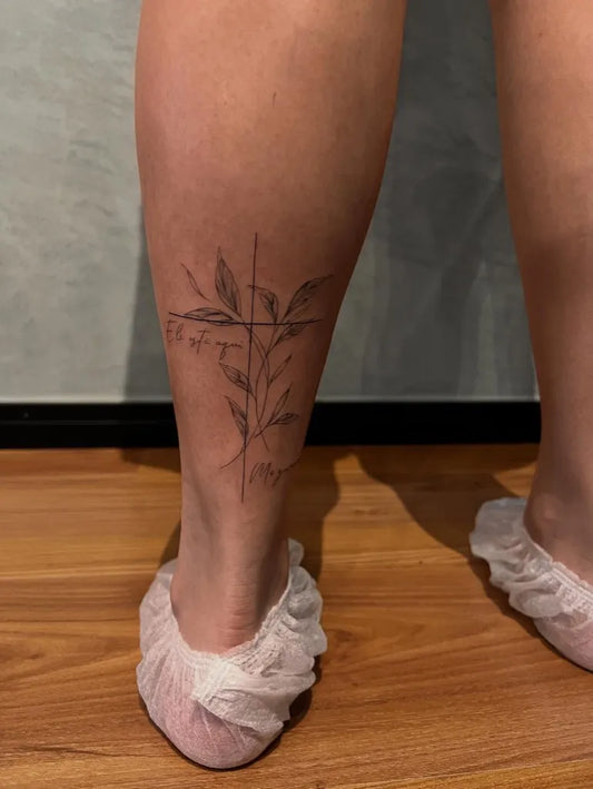 Small Fine Line Cross with Leaves on Women Leg Tattoo by @tonstattoo