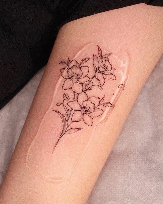 Small Fine Line Daffodil Flowers Tattoo on Women Thigh by @yeowool_tattooer