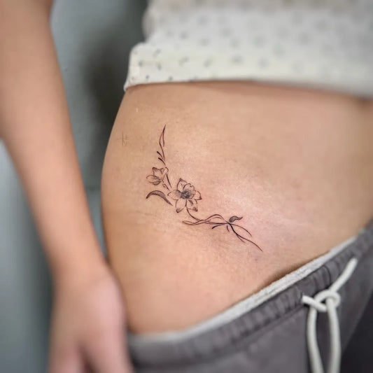 Small Fine Line Daffodil Tattoo on Women Hip by @tatnoir
