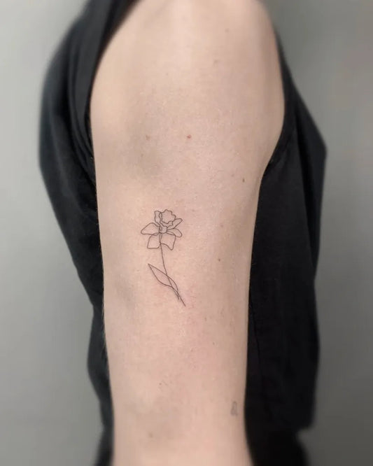 Small Fine Line Daffodil Tattoo on Women Shoulder by @finelinetattooslondon