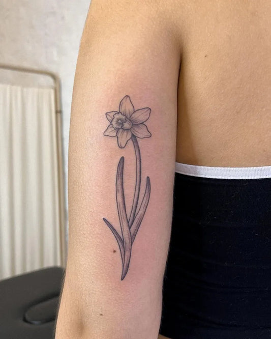 Small Fine Line Daffodil Tattoo on Women Upper Arm by @shanhantattoo