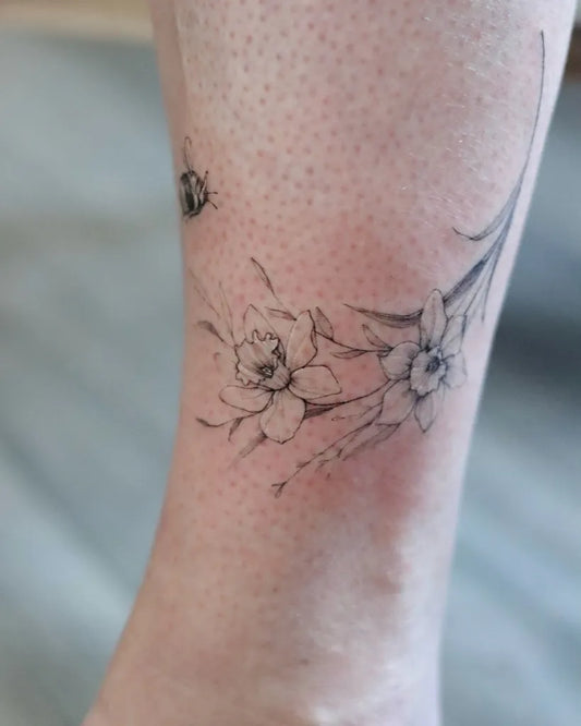 Small Fine Line Daffodil and Bee Tattoo on Women Ankle by @ondo.tattoo