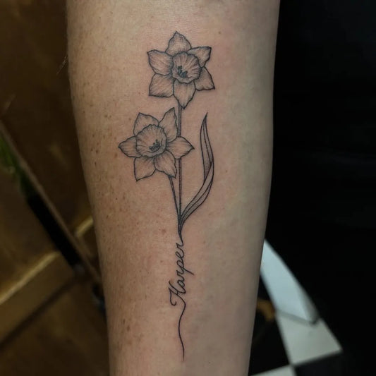 Small Fine Line Daffodil and Name Tattoo on Women Arm by @daynatattoos