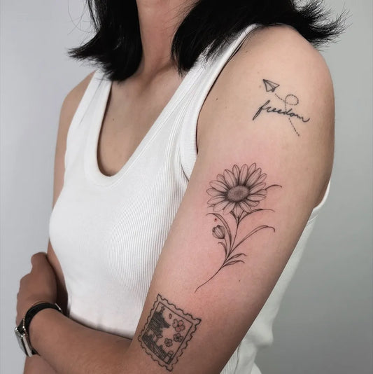 Small Fine Line Daisy Flower and Freedom Word and Stamp Tattoo on Women Shoulder by @damonti.ttt