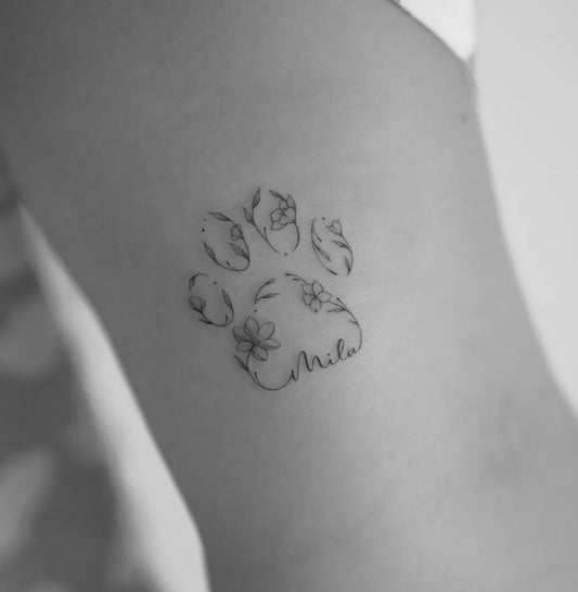 Small Fine Line Dog Paw with Flowers and Name Tattoo on Women Hip by @mrs.tattoo_