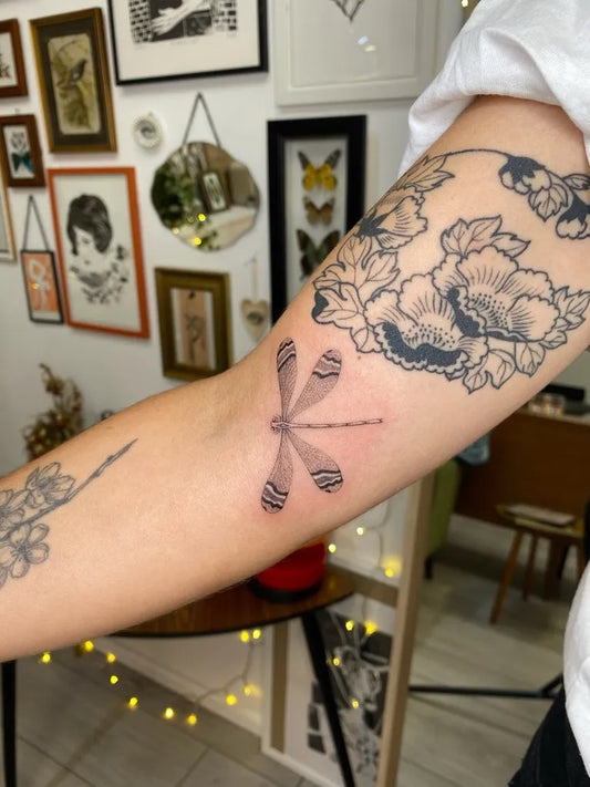 Small Fine Line Dragonfly Flowers on Women Arm Tattoo by @heloisegeslain