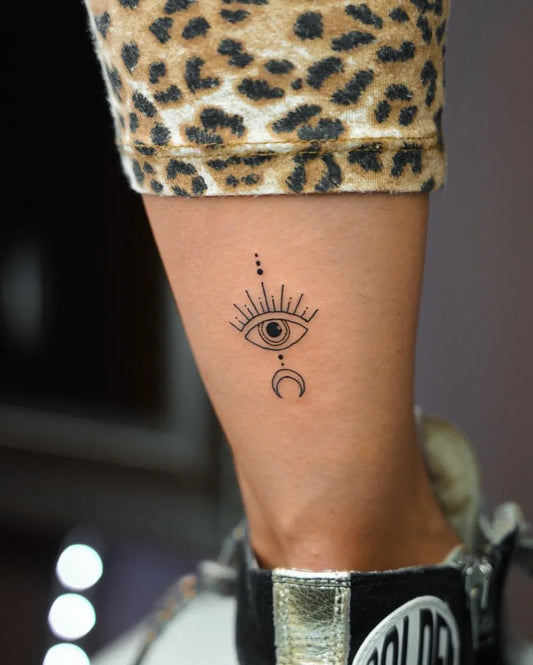 Small Fine Line Evil Eye with Sunburst and Crescent Moon on Women Ankle Tattoo by @sashatattooist