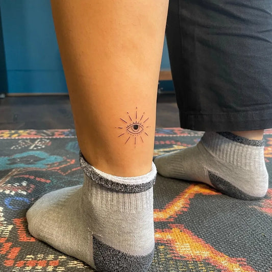 Small Fine Line Eye with Rays on Women Ankle Tattoo by @luciatattoos
