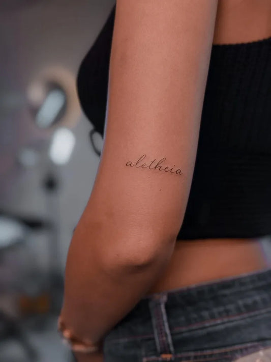Small Fine Line Greek Word on Women Arm Tattoo by @mariposafinelinetattoo