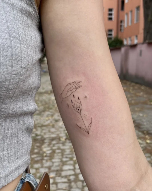 Small Fine Line Hand Holding Flower Tattoo on Women Arm by @vivien.veight