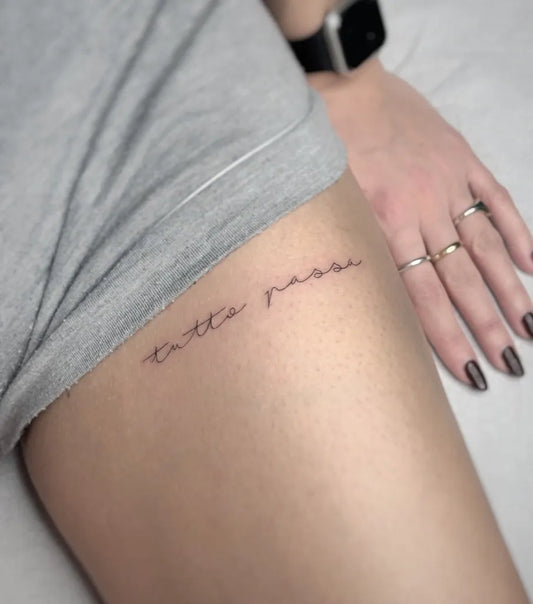 Small Fine Line Italian Phrase Tattoo on Women Thigh by @sailorstattoomilanoduomo