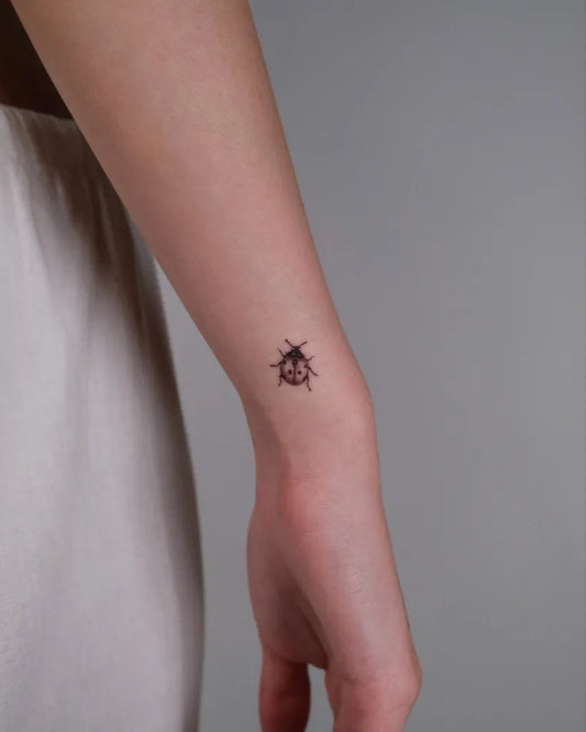Small Fine Line Ladybug Tattoo on Women Wrist by @st0rm.ink