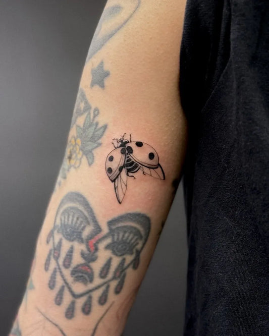 Small Fine Line Ladybug and Flowers Tattoo on Women Arm by @seeroro_ink