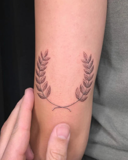 Small Fine Line Laurel Wreath Tattoo on Women Arm by @cachotattoo