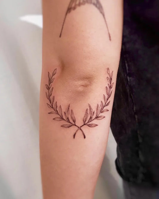 Small Fine Line Laurel Wreath Tattoo on Women Elbow by @neat_tattoo