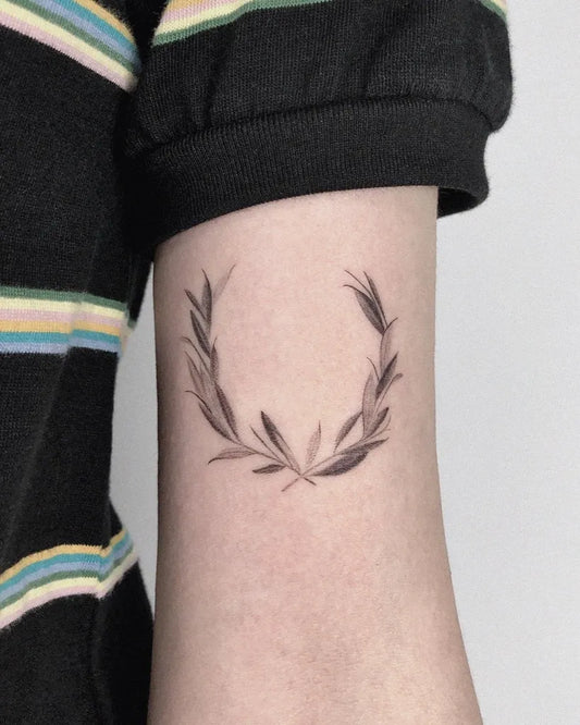 Small Fine Line Laurel Wreath Tattoo on Women Upper Arm by @zezetattoo