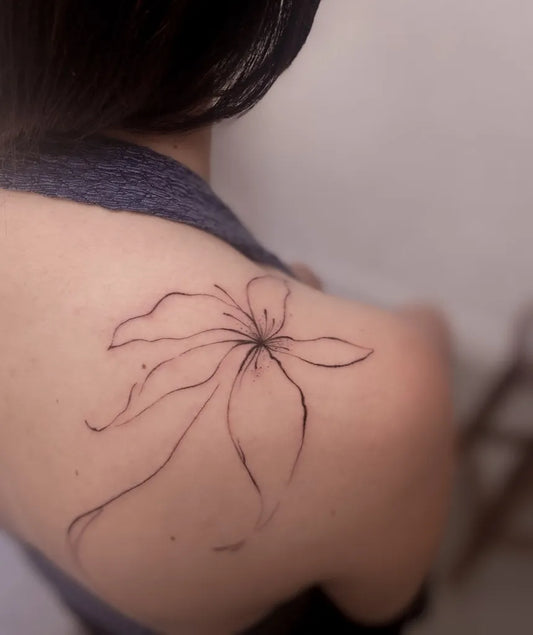 Small Fine Line Lily Flower on Women Shoulder Tattoo by @turkantugcetufan