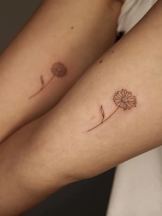 Small Fine Line Matching Daisy Tattoo on Women Arm by @sunami_ink