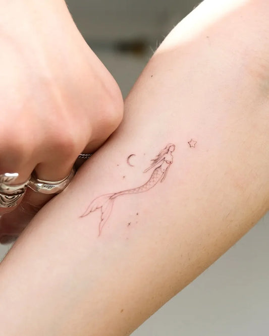 Small Fine Line Mermaid with Moon and Stars Tattoo on Women Arm by @stefano__mazza