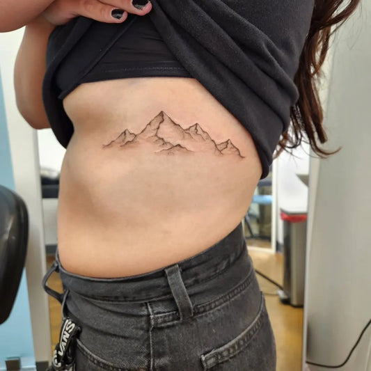 Small Fine Line Mountain Range Tattoo on Women Rib by @kajul_tattoo