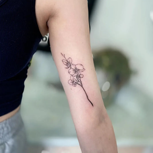 Small Fine Line Orchid Tattoo on Women Upper Arm by @toji_tattoo_studio