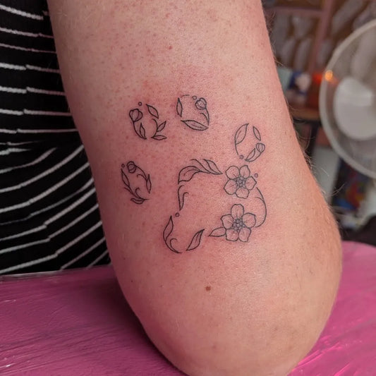 Small Fine Line Paw Print with Flowers Tattoo on Women Arm by @rhithehuman