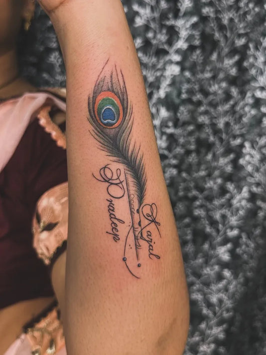 Small Fine Line Peacock Feather with Name Tattoo on Women Arm by @vijaytattooartist