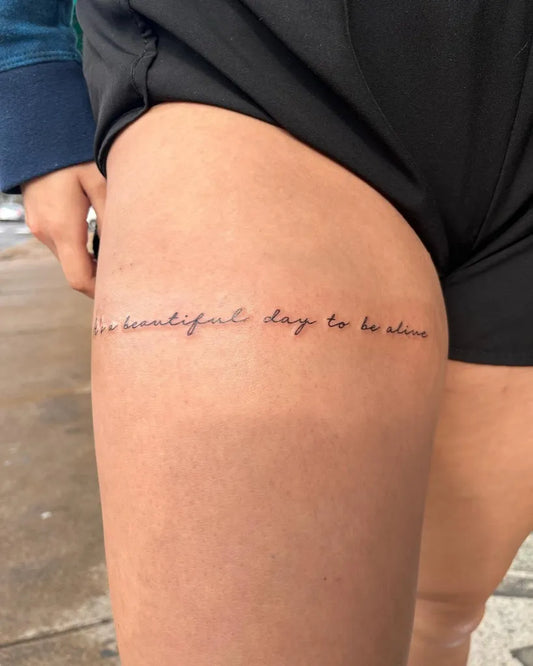 Small Fine Line Script Quote Tattoo on Women Thigh by @azratattoos
