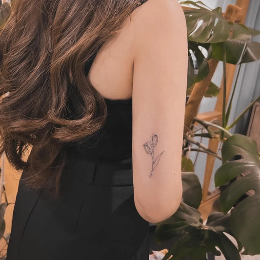 Small Fine Line Tulip Tattoo on Women Upper Arm by @sherrie_inlayerink