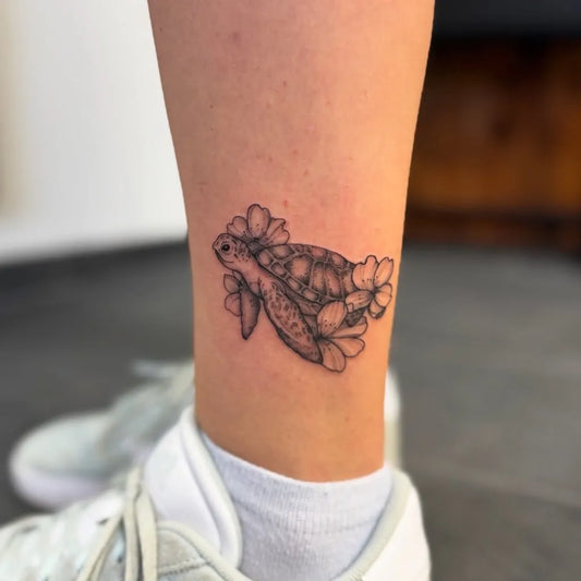 Small Fine Line Turtle and Hibiscus Tattoo on Women Ankle by @bavariatattoo