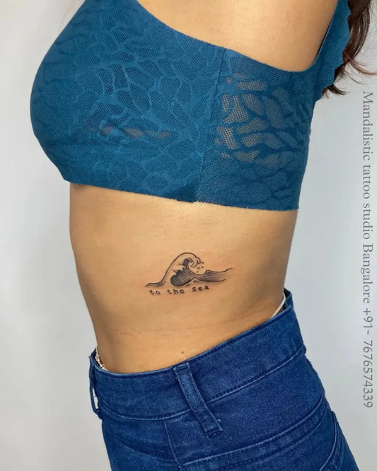 Small Fine Line Wave and Text Tattoo on Women Side by @mandalistictattoostudio
