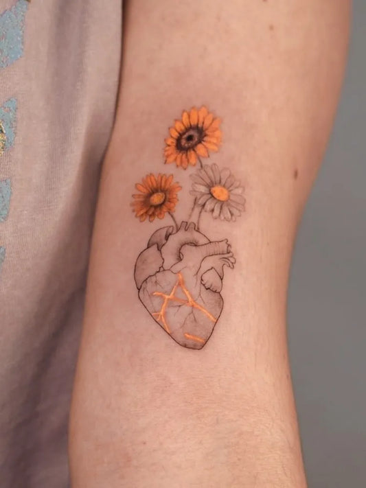 Small Fine Line Yellow Daisy Anatomical Heart Tattoo on Women Arm by @chiara.guu