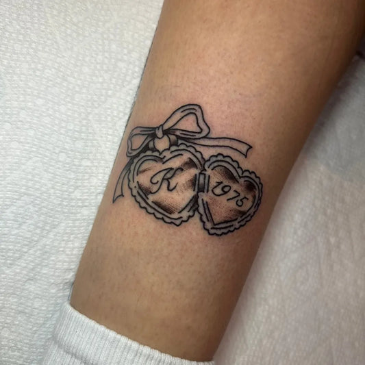 Small FineLine DoubleHeartLocketWithRibbon on Women Arm Tattoo by @selfcaretattooco
