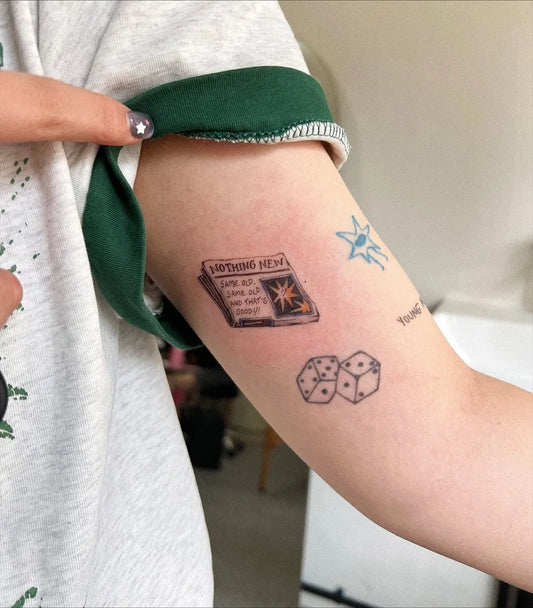 Small Illustrative Newspaper and Dice Tattoo on Women Arm by @nothin.tooit