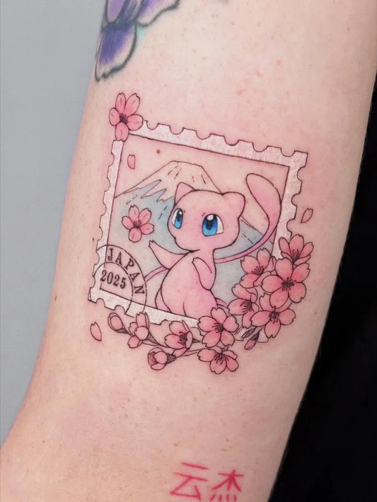 Small Illustrative Pink Pokemon Mew Stamp Tattoo on Women Arm by @pokemon.tatts