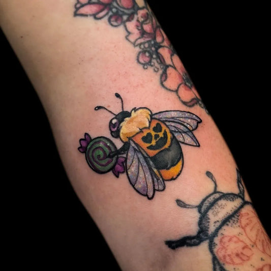 Small Illustrative Pumpkin Bee with Candy on Women Arm Tattoo by @morninggorytattoo
