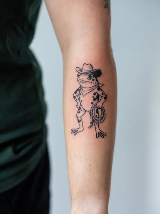 Small Linework Cowboy Frog Tattoo on Women Forearm by @annedekkertattoo