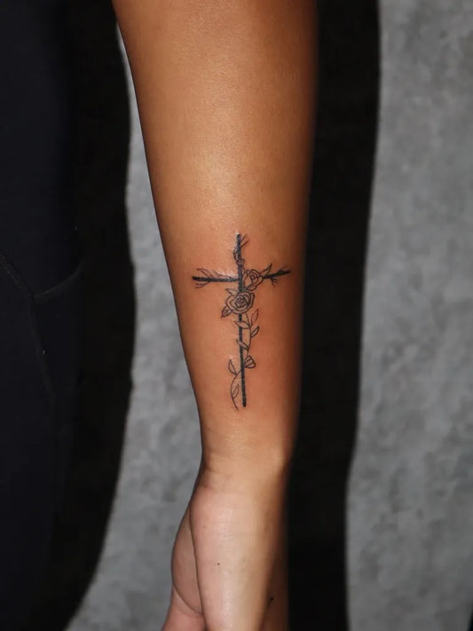Small Linework Cross with Flowers on Women Arm Tattoo by @wasem.tattoo