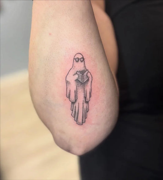 Small Linework Ghost with Book Tattoo on Women Arm by @skynn.studio