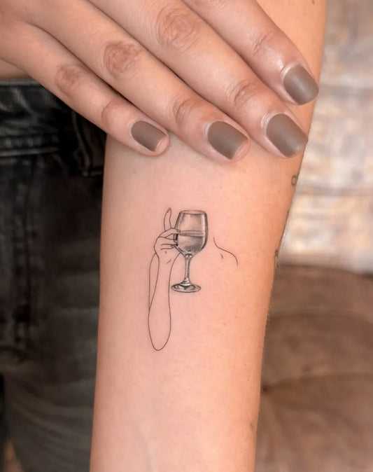 Small Linework Hand Holding Wine Glass on Women Arm Tattoo by @tayeh.studio