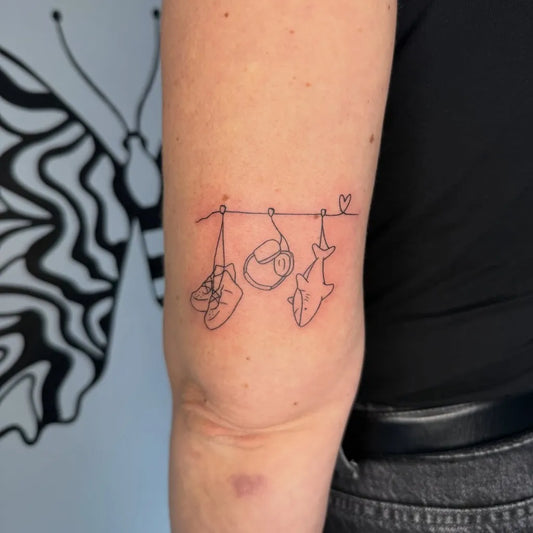 Small Linework Hanging Shark and Shoe Family Tattoo on Women Arm by @booom.tattoo