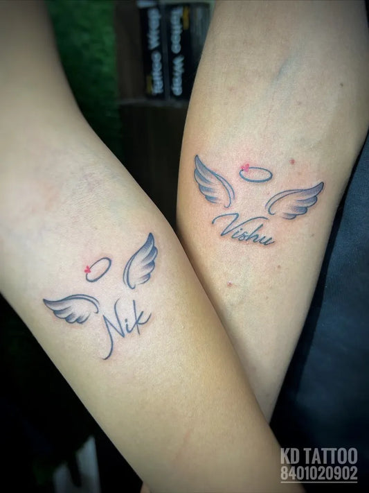 Small Matching Angel Wings with Halo and Name Tattoo on Women Wrist by @kd_tattoo_saloon