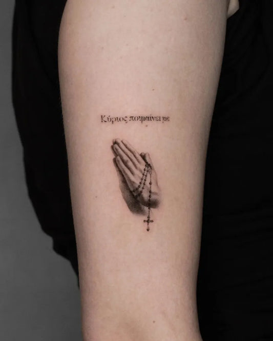 Small Micro Realism Praying Hands with Rosary and Greek Text on Women Arm Tattoo by @nana.rezy