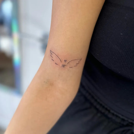 Small Minimalist Angel Wings Tattoo on Women Arm by @taylorstinytattoos