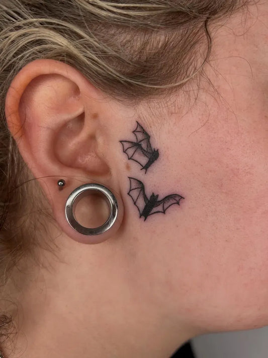 Small Minimalist Bat Tattoo on Women Face by @poppyoliviatattoo